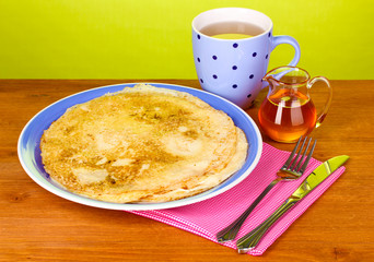Stack of tasty pancakes on wooden table on green background