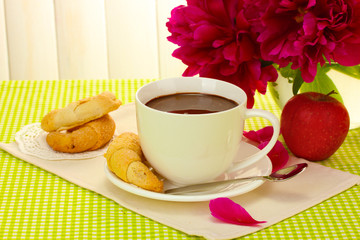 cup hot chocolate, apple, cookies and flowers on table in cafe