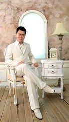 Chinese young man in white suite sitting in chair in bright room