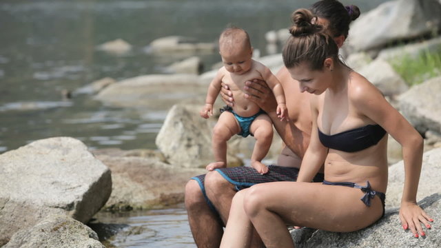 young parents with little baby dangling their legs in the lake