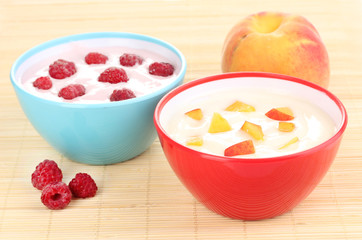 Yogurt with peaches and raspberries in bowls on bamboo mat