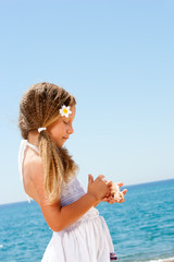 Cute girl holding shells on sunny beach.