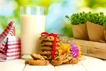 glass of milk, chocolate chips cookies with red ribbon and