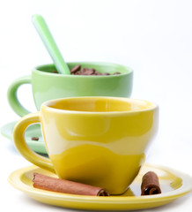 Green and yellow cup with coffee beans and two cinnamon sticks