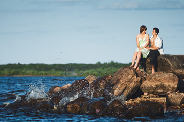 couple sitting on shore of lake, where wave beats on rocks