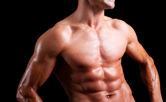 Young muscular man with beautiful torso agaisnt black background