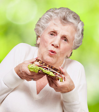 portrait of senior woman holding a delicious sandwich against a