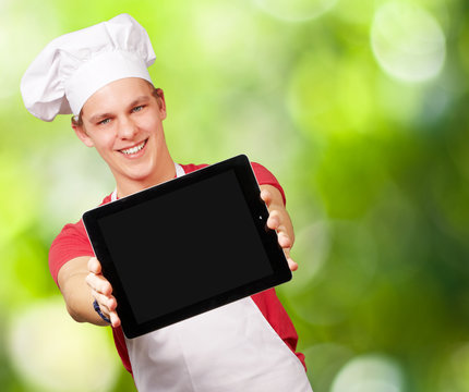 portrait of young cook man showing a digital tablet against a na