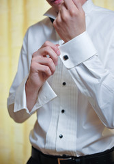 A groom putting on  cuff-links as he gets dressed in formal wear