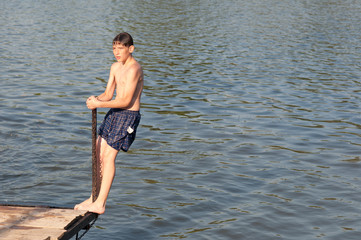 Fototapeta na wymiar Teenage boy jumping in the river from the dock