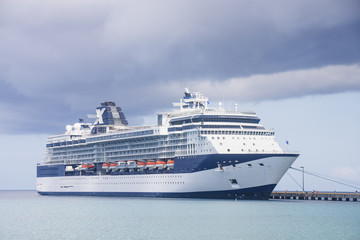 Fototapeta na wymiar Blue and White Cruise Ship Tied to Pier Under Cluds