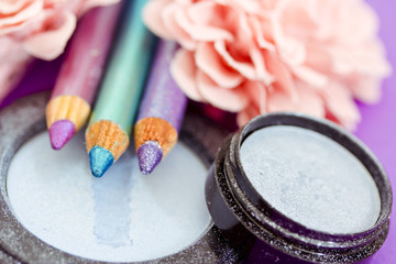 eyepencils and eyeshadows on purple with petals