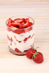 Glass of ripe strawberries with cream on wooden background