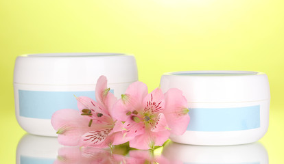 Obraz na płótnie Canvas Jars of cream with flower on green background