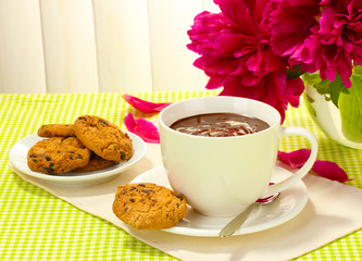 cup hot chocolate, cookies  and flowers on table in cafe