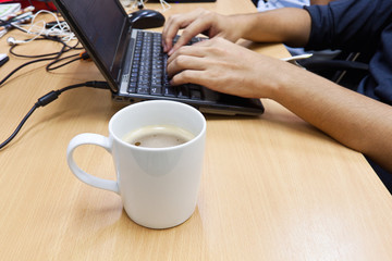 Cup of coffee with hand on laptop