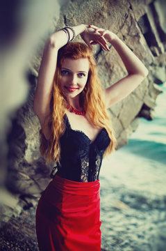 The beautiful red-haired girl poses on a sandy beach