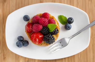fruit cake with berries on white plate with a fork, top view