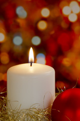 Cream candle, gold tinsel, bauble and blurred light background