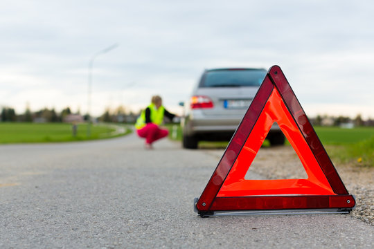 Junge Frau mit Warndreieck auf Stra&szlig;e