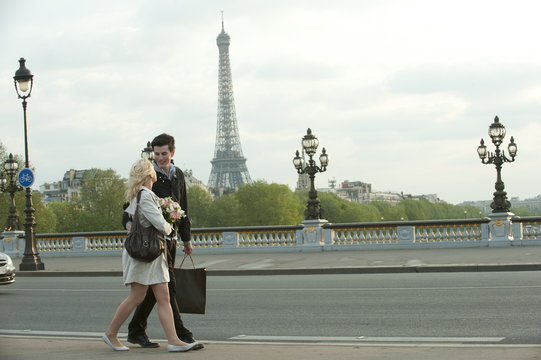 Caucasian couple walking across bridge with Eiffel Tower in background