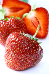 Strawberries on white background, one of them is sliced in half