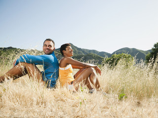Couple sitting back to back in field after exercise