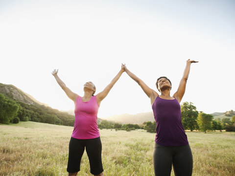 Athletic women standing in field with arms raised