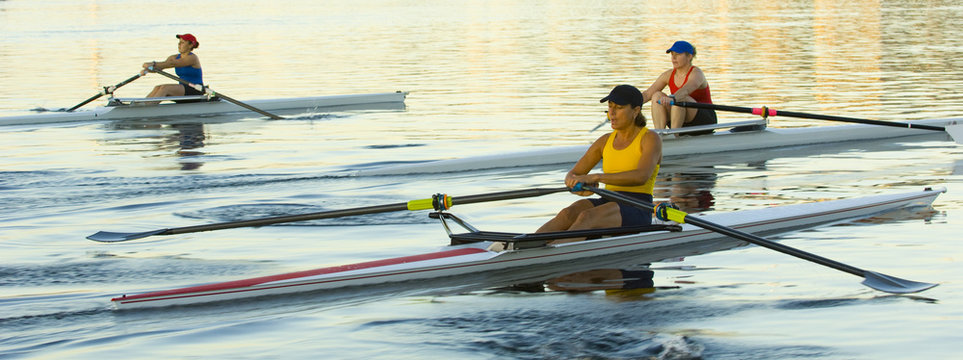 People rowing sculling boats on river