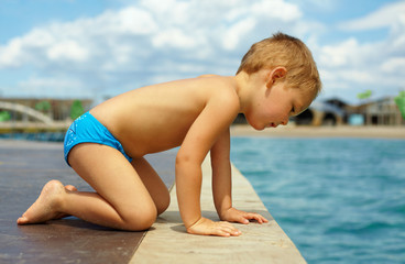 cute kid squats on pier, looks in water