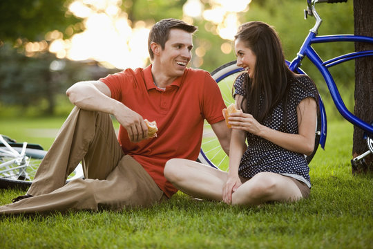 Caucasian couple sitting in grass eating lunch