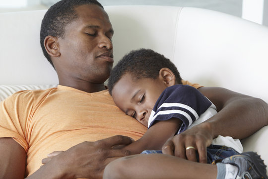 African American father napping on sofa with son