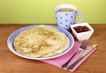 Stack of tasty pancakes on wooden table on green background