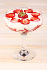 Glass of ripe strawberries with cream on wooden background