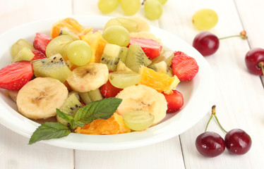 Fresh fruits salad on plate and berries on white wooden table