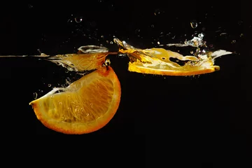 Poster Zwei Segmente von reifen Orangen, die mit Spritzen ins Wasser fallen © Boris Bulychev