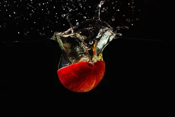 Zelfklevend Fotobehang Gehalveerde verse appel die met een plons in het water valt © Boris Bulychev