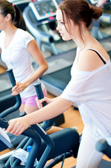 Fototapeta premium Two young sporty women run on machine