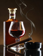 bottle and glass of brandy and cigar on brown background