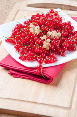 Glass plate full of ripe red currant on a wooden board