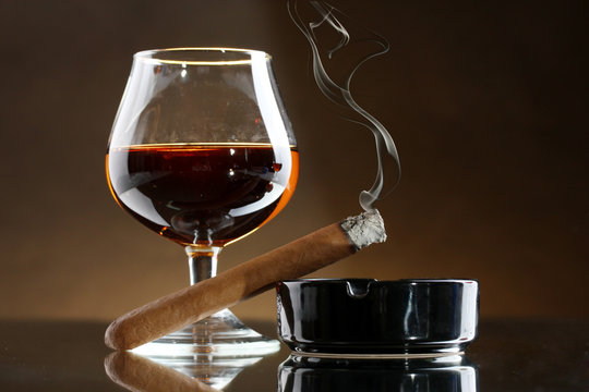 glass of brandy and cigar on brown background