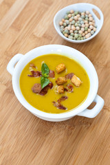 A bowl of pea cream soup with croutons and bacon