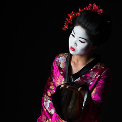 Portrait of geisha presenting something isolated on black