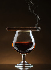 glass of brandy and cigar on brown background