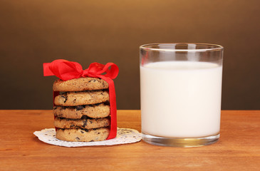 Glass of milk and cookies on wooden table on brown background