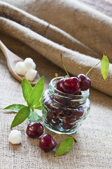 Red cherries in glass jar on sackcloth