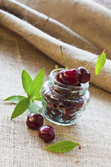 Red cherries in glass jar on sackcloth