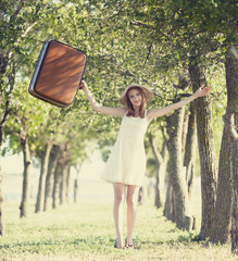 Redhead girl with suitcase at tree's alley.