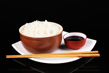 Bowl of rice and chopsticks on plate isolated on black