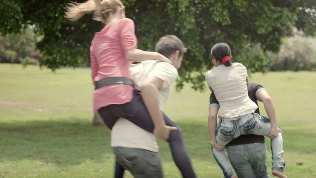 Friends having fun, young couples running piggyback in city park